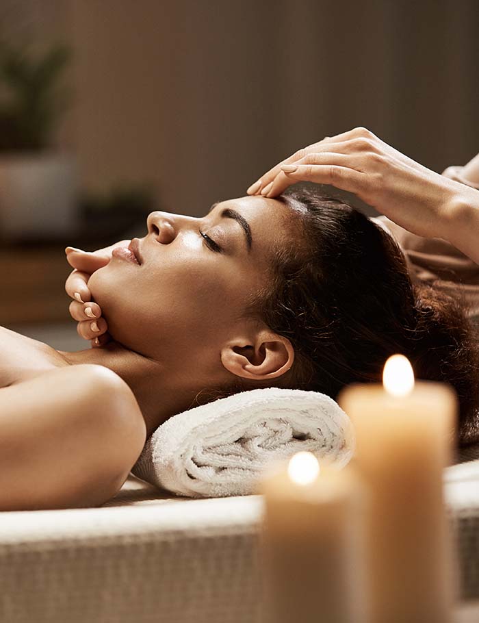 Attractive african girl enjoying face massage in spa salon.